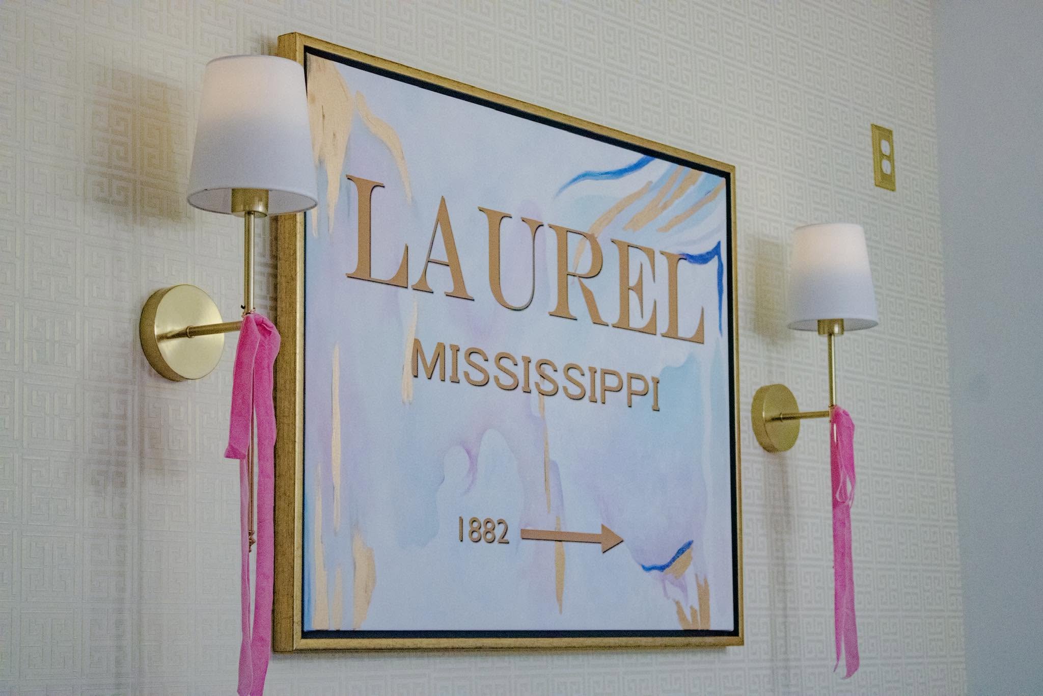 Decorative sign with 'Laurel, Mississippi' on a wall with two lamps.